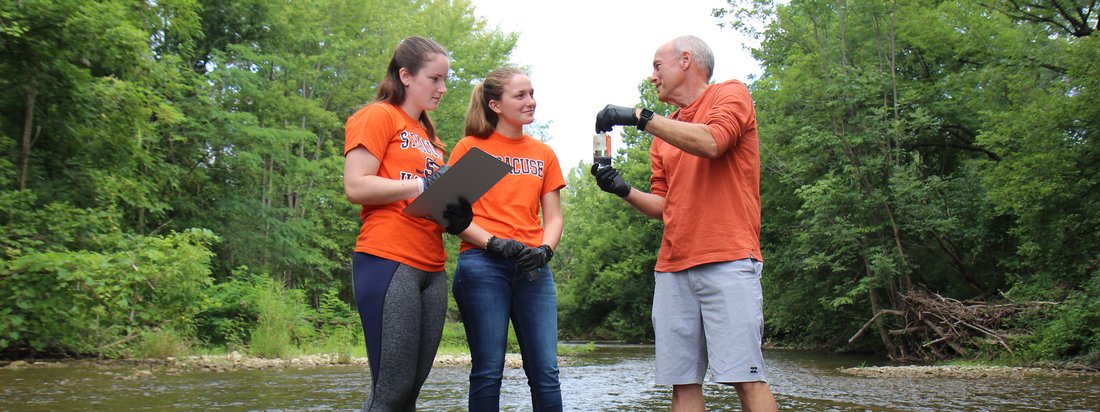 Three people collecting samples from a river.