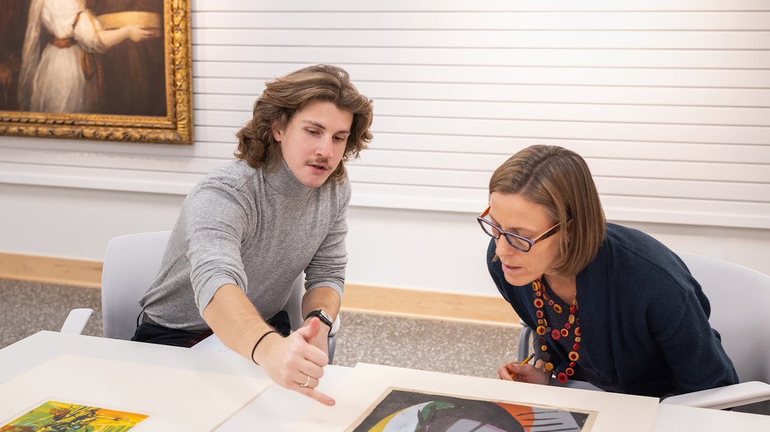 Sascha Scott sitting with a student and looking at art on a white table.