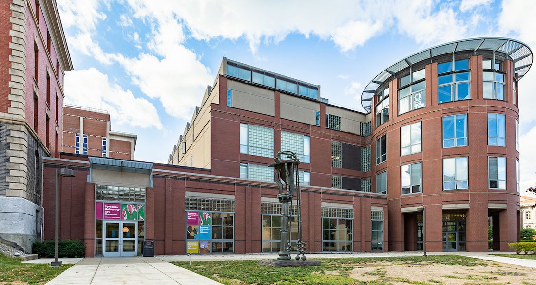 An image of the Syracuse University Art Museum. A large metal art installation stands in front of the museum.