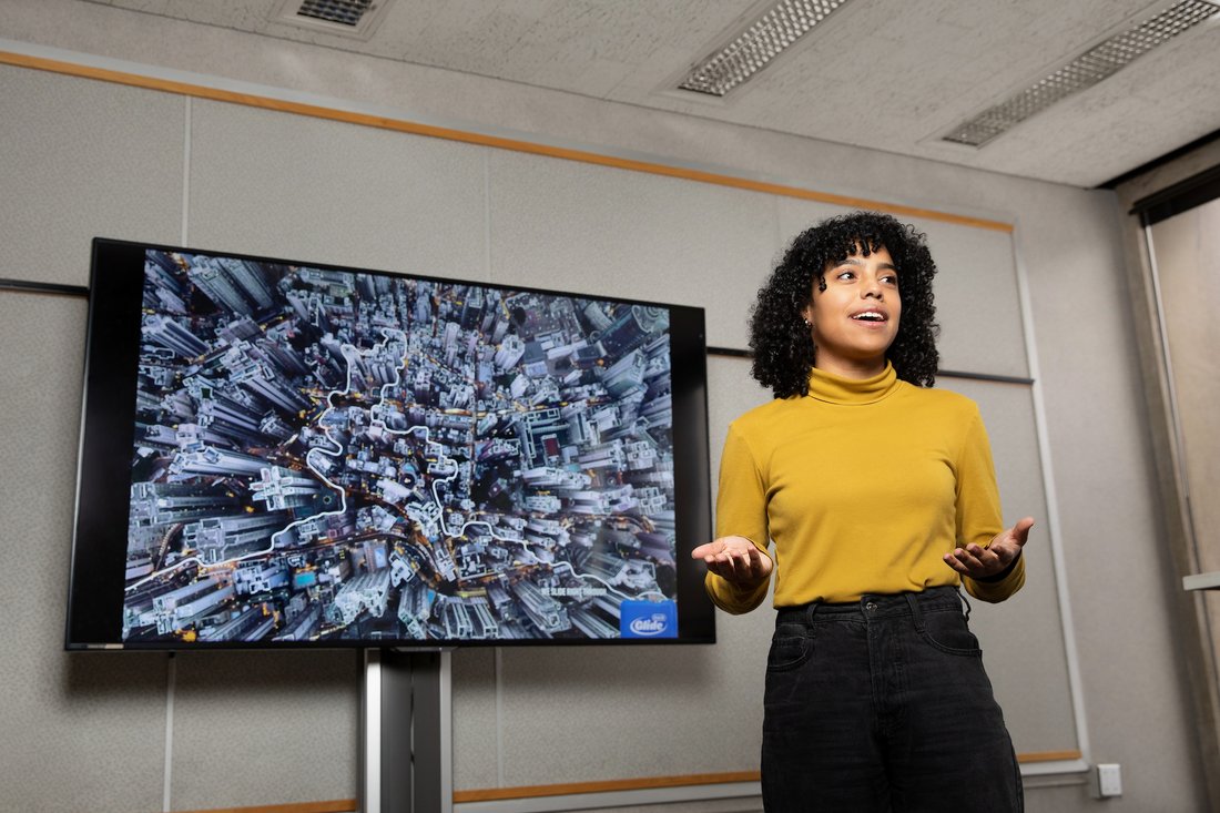 A woman delivers a class presentation in front of a video screen