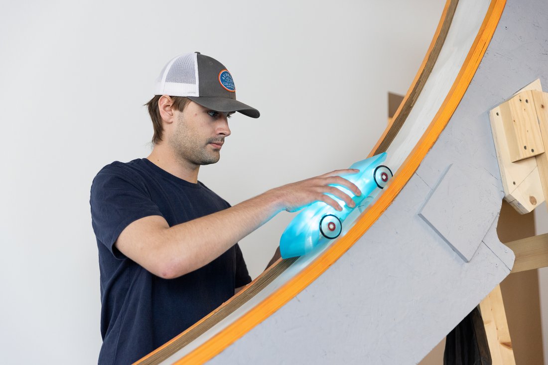 A student holds a toy car on a curved ramp