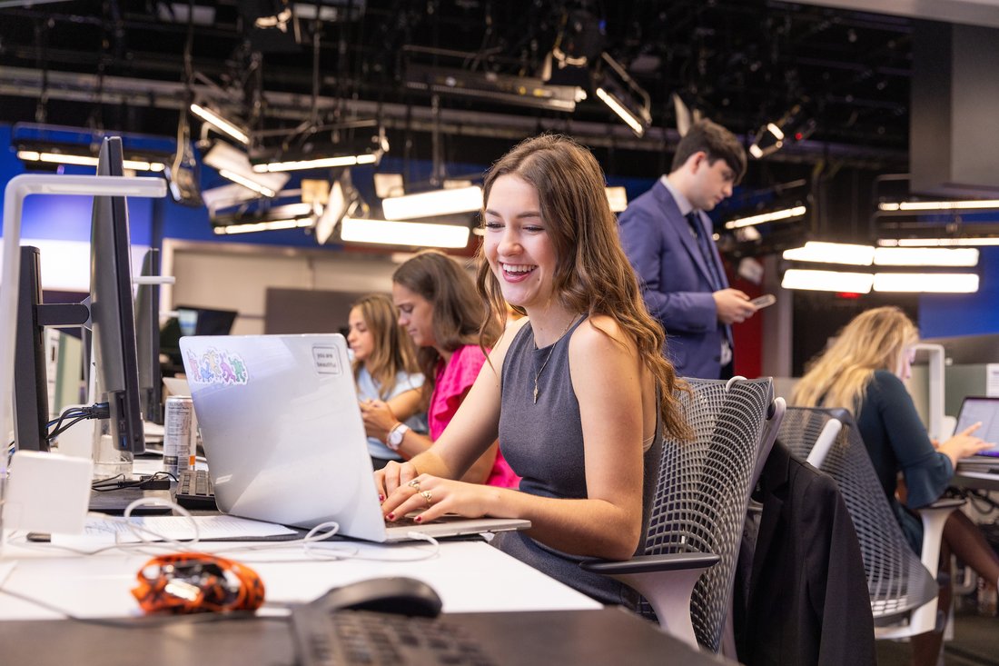 Female student works at a computer in the Newhouse studio during a news production class