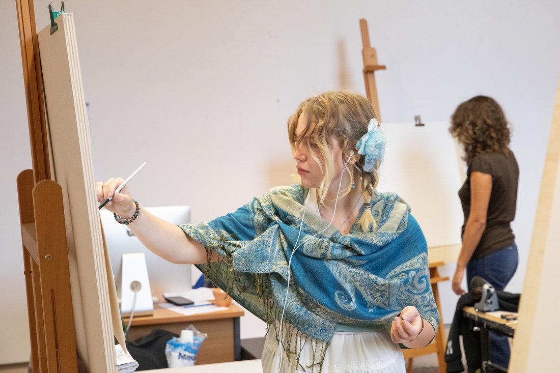 A person stands at an easel and sketches on a canvas.