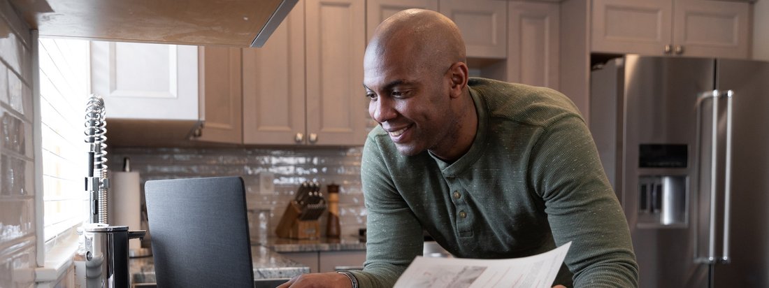 Joesph Jasper on his computer and flipping through a book in his kitchen.
