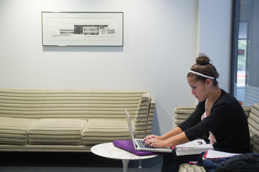 Woman sits in lounge and types on laptop