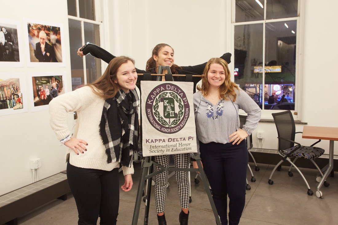 three student pose with their arms up in front of a kappa delta pi banner