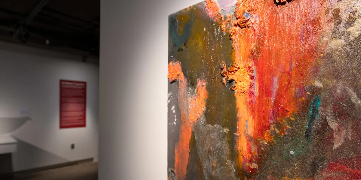 An abstract painting of orange, yellow and green colors hangs on a wall.