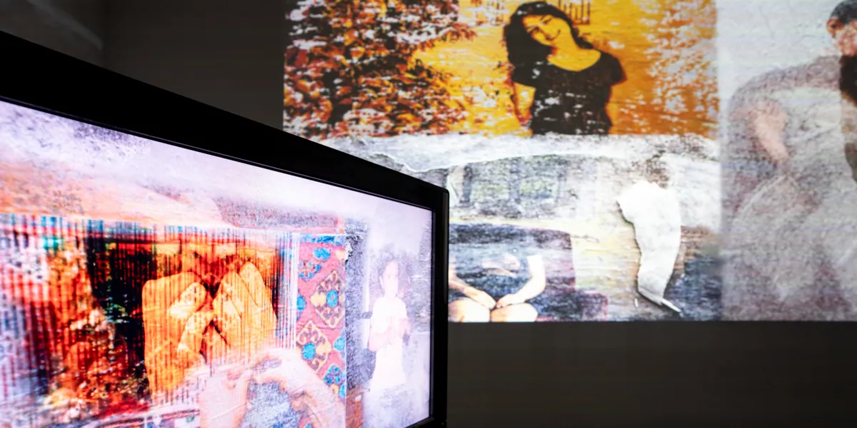 A television screen showing a film made up of colorful photographs. On the wall is projected a yellow image of a woman smiling.