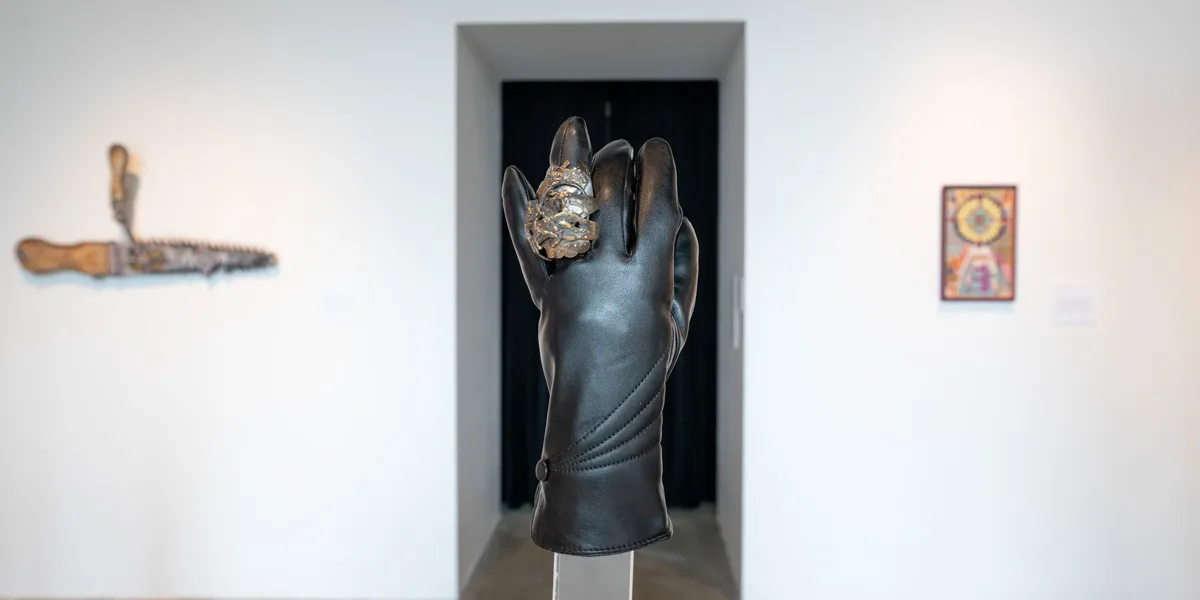 A black glove on a pedestal. A large, metal, oval ring is on one finger.