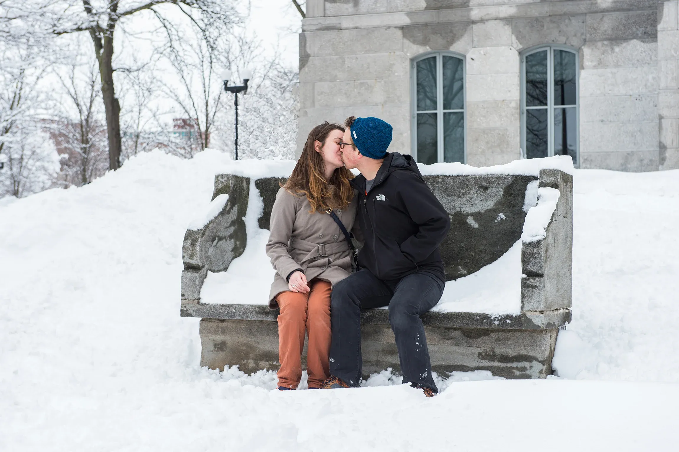 Two students kissing on bench in the snow.