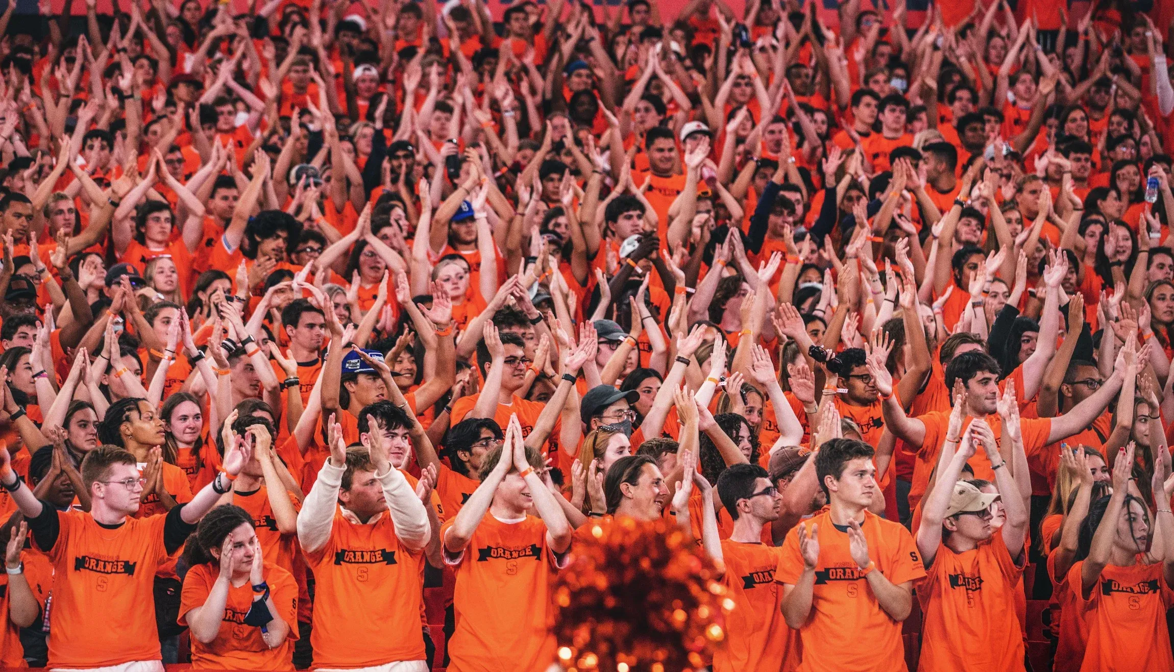 A large group of students wearing orange shirts cheering.